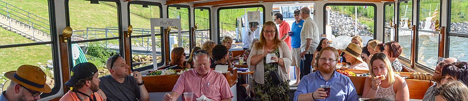 Banner of a group of cruisers onboard the River Cruiser, eating, drinking, and talking on a sunny day.