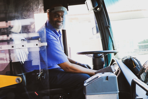 Closeup of a EMBARK Transit professional wearing a face shield and driving inside a fixed-route bus.