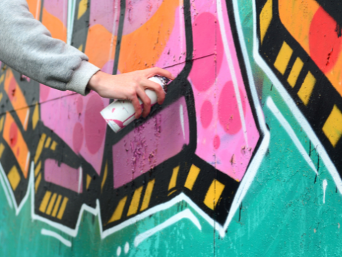 Person spray painting a colorful wall mural.