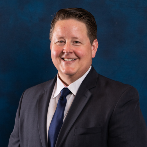 Headshot of IT Manager Michael Scroggins with blue background.